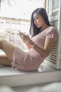 Young woman using her smartphone on a windowsill