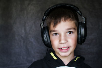 Close-up portrait of boy listening music in headphones against wall