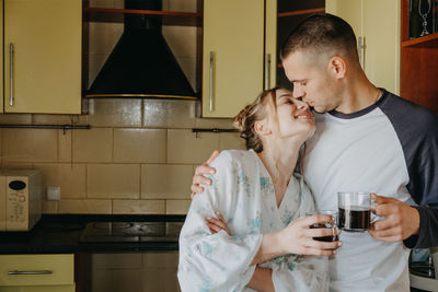 Couple holding coffee cup embracing in kitchen