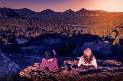 Rear view of female friends looking at mountains while relaxing on rock