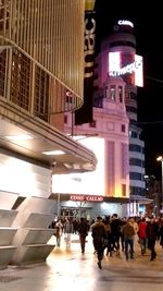 People walking on illuminated street in city at night