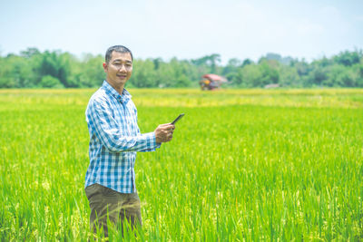 Portrait of man standing on field while using digital tablet