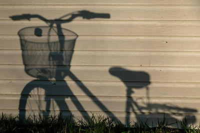 Shadow of bicycle on footpath against wall