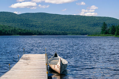 Boat moored by pier over lake against green mountains