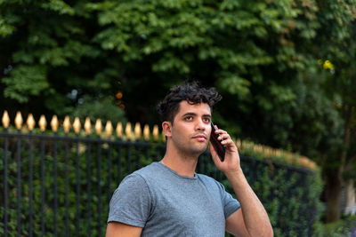 Portrait of young man looking away while standing against trees