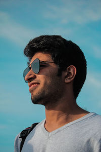 Smiling young man wearing sunglasses against blue sky