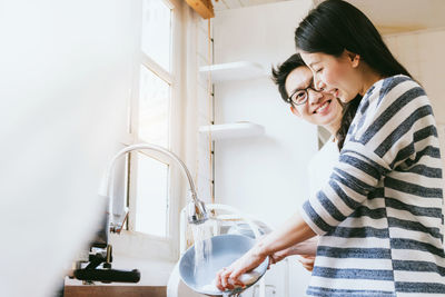 Smiling man looking at woman washing plate in kitchen