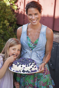 Portrait of mother and daughter, woman holding cake