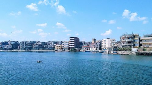 Sea by buildings against blue sky