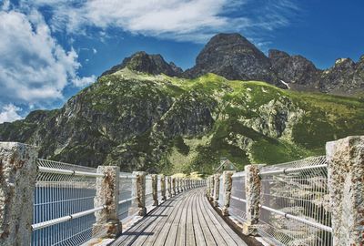 Footbridge over mountain against cloudy sky