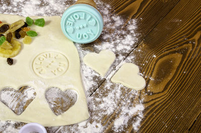 Hearts of dough, dried fruits and print love on wooden background.