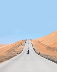 Person standing on country road in desert against clear blue sky