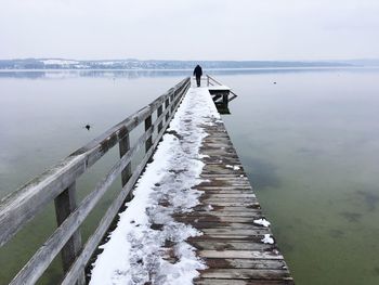 Woman walking on pier at sea against sky during winter
