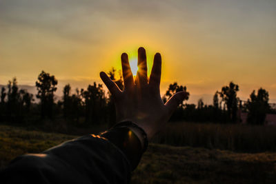 Cropped hand covering sun in sky during sunset