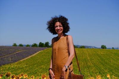 Portrait of smiling woman standing at sunflower farm against clear blue sky