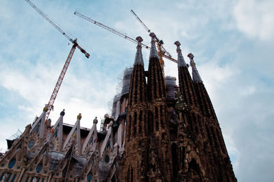 Low angle view of cranes against sagrada familia and sky, barcelona 
