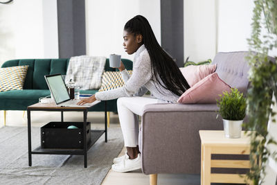 Female entrepreneur drinking coffee while using laptop at home