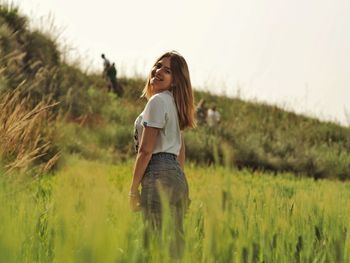 Portrait of young woman standing on grass against sky