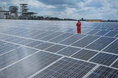 Manual worker working amidst solar panels against sky