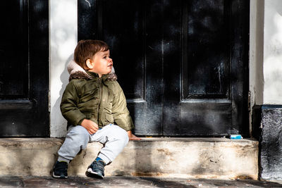 Cute boy sitting by closed house door