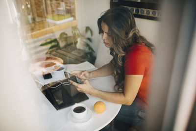 Freelancer female using phone seen through glass window