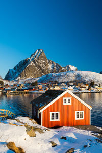 Houses by mountain against clear blue sky during winter