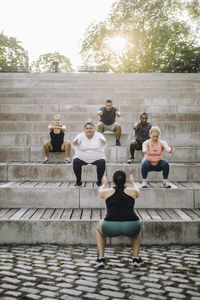 Team doing squats on steps with female fitness instructor at park