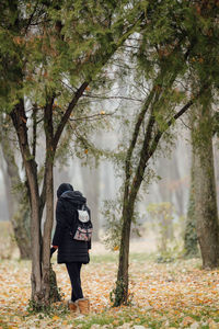 Rear view of man standing amidst trees in forest