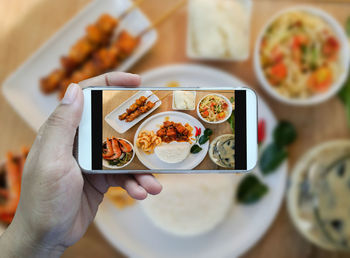 Cropped hand of person photographing food through smart phone