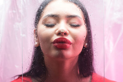 Close-up of young woman kissing wet glass