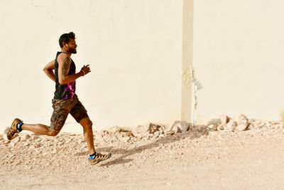 Side view of young man running by building