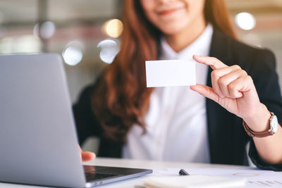 Midsection of businesswoman holding business card in office