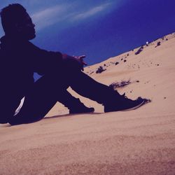 Silhouette man sitting on sand at beach against clear blue sky