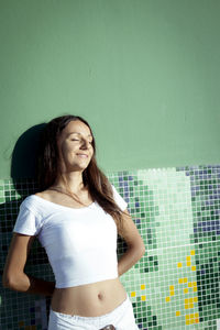 Woman dressed in white leaning on green wall. positive and smiling attitude