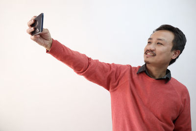 Man holding camera while standing against white background