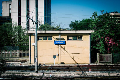 Information sign on railroad tracks by building against blue sky