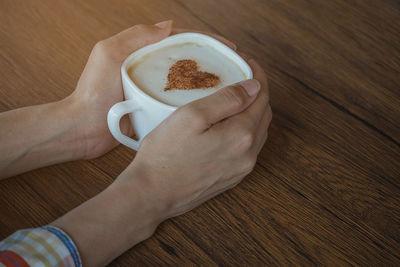 Close-up of hand holding coffee cup on table