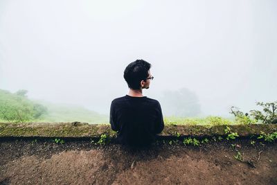 High angle view of man sitting on observation point during foggy weather