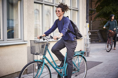 Smiling young female architect riding bicycle on street in city