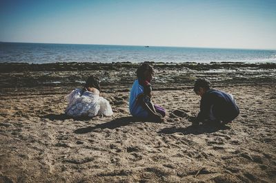 Rear view of women sitting on beach against sea