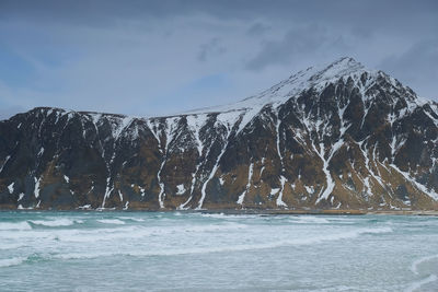 Scenic view of sea by snowcapped mountains against sky