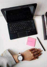 Cropped hand of woman wearing wristwatch with laptop on table