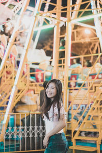 Portrait of smiling young woman standing at amusement park during night