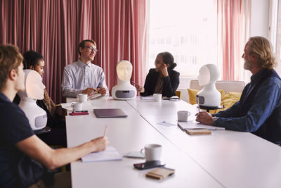 Business people discussing robot voice assistant during meeting