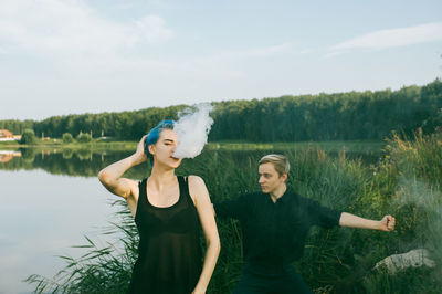 Woman exhaling smoke while standing by friend at lakeshore