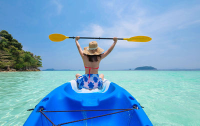 Rear view of young woman sitting in boat on sea against sky