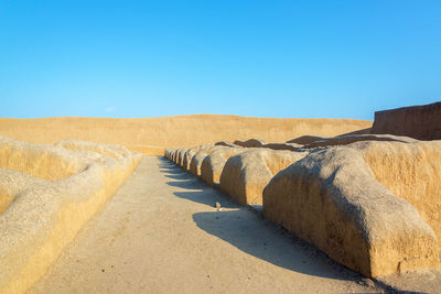 Pathway amidst adobe walls of ancient city against clear blue sky