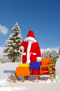 Man in costume with gifts standing on snow against sky