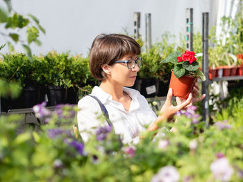Woman chooses plants for landscaping. outdoor shelves with seedlings and seeds in flower shop. 