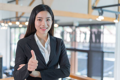 Portrait of confident businesswoman gesturing thumbs up in office